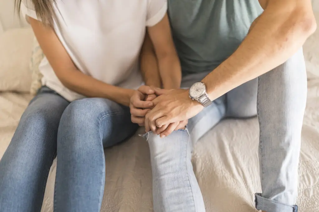 Two people sitting on a bed holding hands